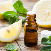 Essential lemon oil in bottle, fresh fruit slices on wooden background. Natural fragrances.